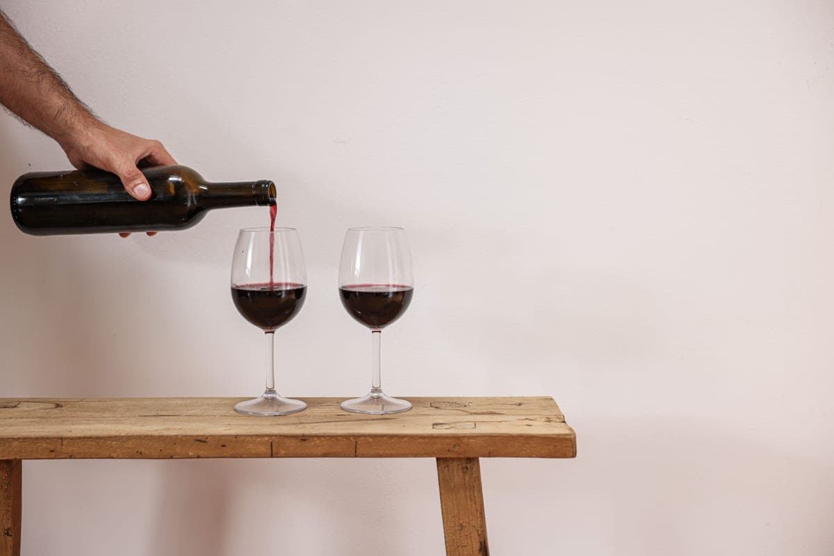 Red wine being poured into glasses on a wooden table