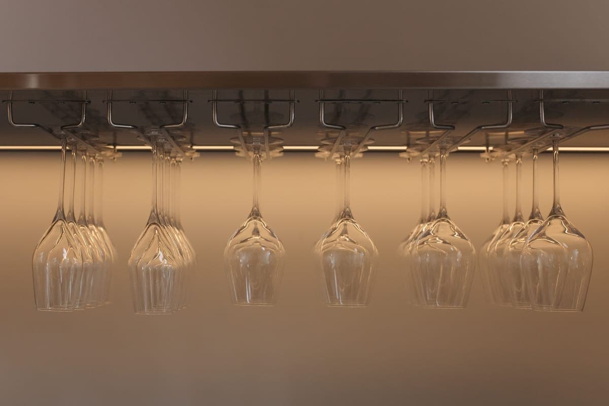 Wine glasses hanging upside down from a stainless steel under-cabinet rack